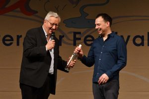 Festivalleiter Dr. Josef Zierden schenkte dem Bestsellerautor eine Flasche Eifel-Geist. Bild: Harald Tittel/ELF