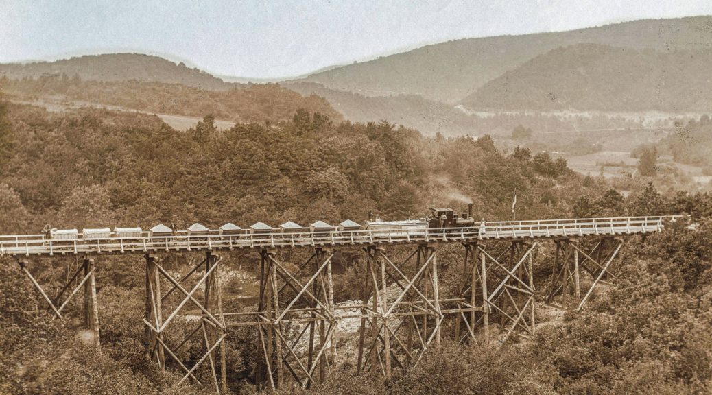 Die Holzbrücke über das Lorbachtal. Im Verlauf der Arbeitsbahn gab es mehrere dieser Holzbrücken, über die der Bahn- und Fußgängerverkehr zur Baustelle geführt wurde. Mit der Zeit wurden die Holzkonstruktionen durch Steindämme ersetzt, über die heute noch die K 7 führt. Bild: AWVER