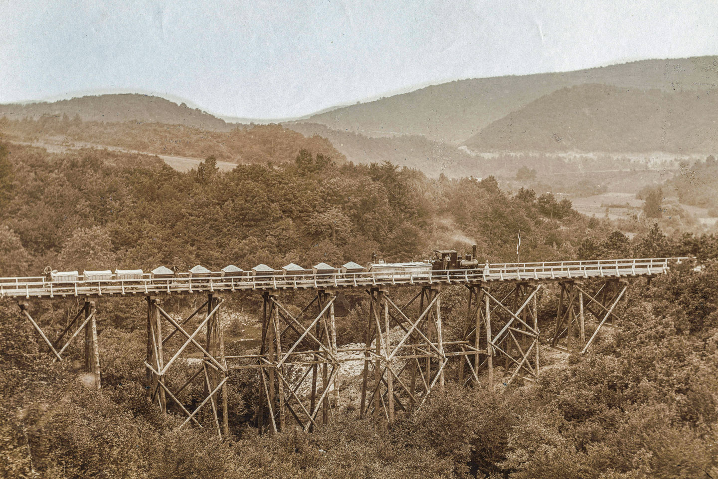 Die Holzbrücke über das Lorbachtal. Im Verlauf der Arbeitsbahn gab es mehrere dieser Holzbrücken, über die der Bahn- und Fußgängerverkehr zur Baustelle geführt wurde. Mit der Zeit wurden die Holzkonstruktionen durch Steindämme ersetzt, über die heute noch die K 7 führt. Bild: AWVER